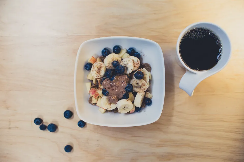 Desayuno con un bol de yogur, fruta y una taza de café sobre una mesa de madera