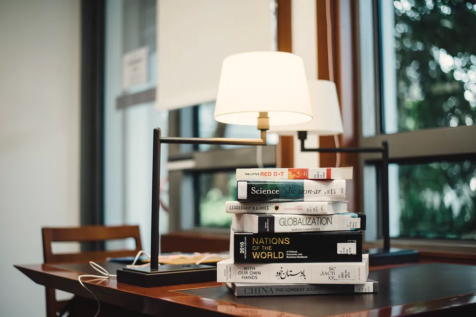 Pila de libros junto a una lámpara de mesa